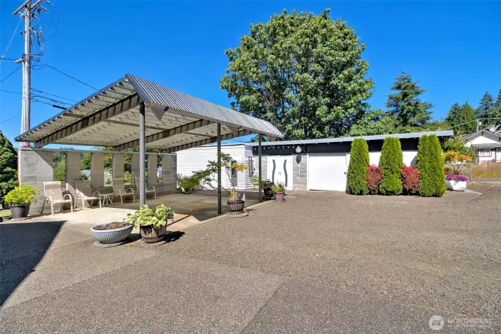 Covered patio with detached 2-car garage and woodshed in background.