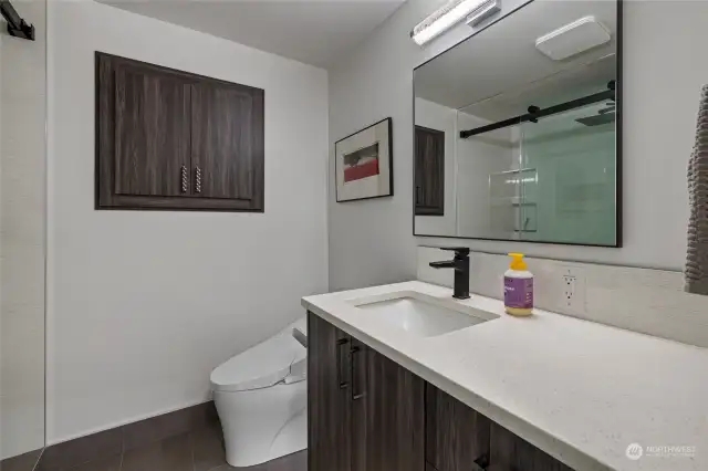 Lower level 3/4 bath features floating vanity with motion light below, toilet/bidet, tile floors & tiled shower.