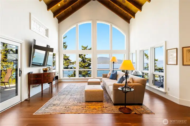 As evening falls, the family room transforms with a warm glow while the windows frame shifting skies and reflections across the water.