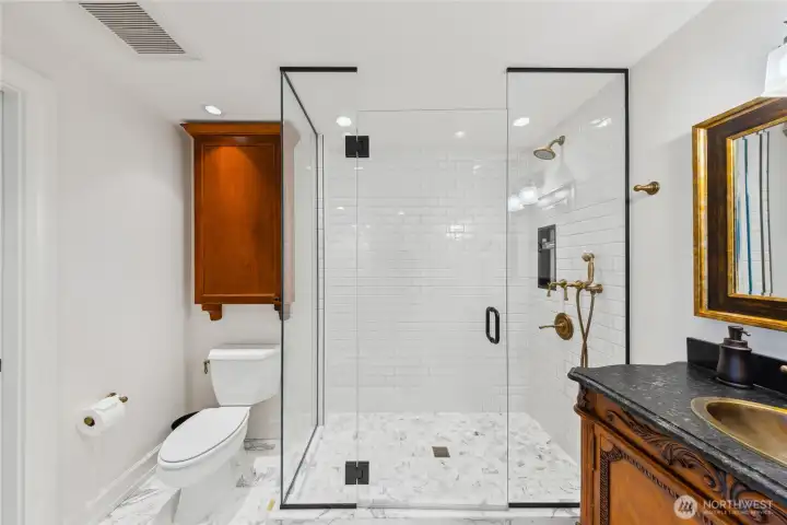 A Carrara marble bath finished with a frameless glass shower, brass fixtures, and a custom carved vanity blends classic materials with modern design.