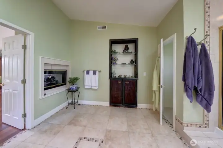 Primary bath with two-way fireplace, built in cabinets/glass shelves and door to water closet.