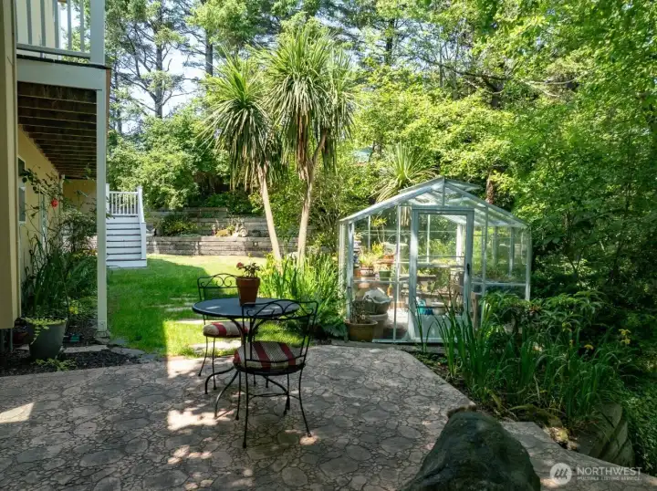 Backyard has a terraced patio and greenhouse with electricity. Notice back yard staircase to deck and home entrance.