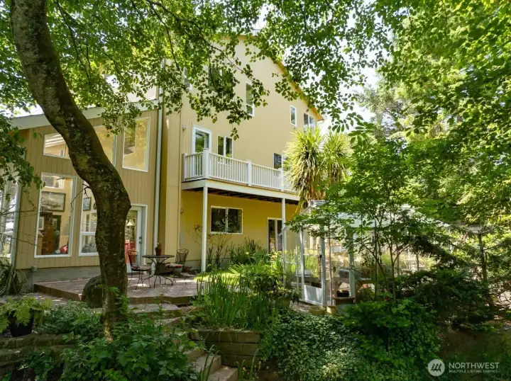 View of the Sunroom, deck on back of house, patio, greenhouse, stairs to lower-level yard in front of photo.