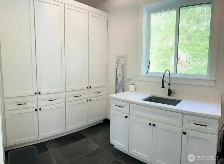 Large mudroom with 4 sets of oversized custom cabinetry to keep items contained, plus a quartz countertop and undermount sink and washer/dryer.