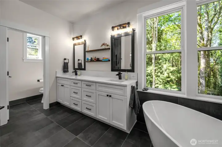 Beautiful primary spa like bath with corner windows to enjoy the nature and matching porcelain tile to the fireplace connects the spaces. Beautiful primary spa like bath with corner windows to enjoy the nature and matching porcelain tile to the fireplace connects the spaces.
