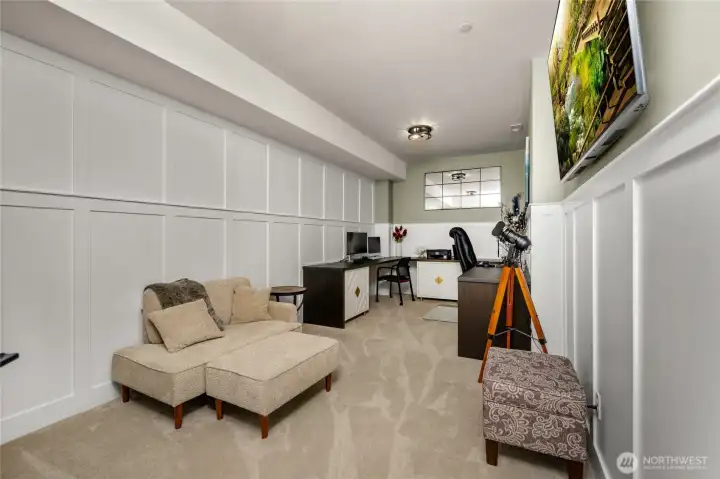 Additional room/office space in basement with floor-to-ceiling wainscoting and built-in U-shaped desk with storage cabinets.