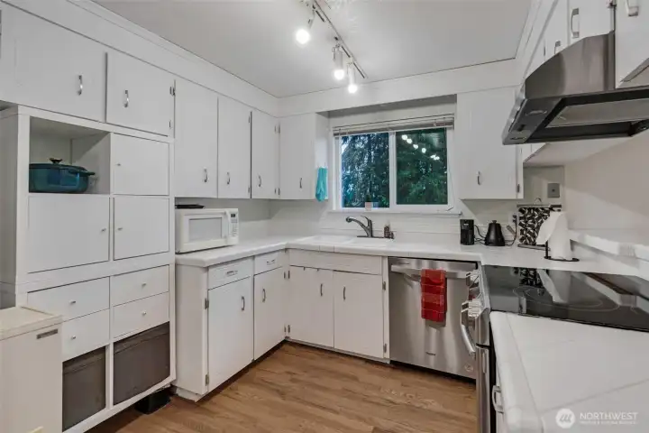 A well-functioning kitchen offers bright white ceramic tile countertops and cabinets with loads of storage space.