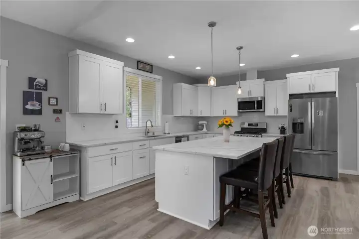 Upgraded kitchen with quartz counters, white cabinetry, stainless appliances, gas range, and large center island.