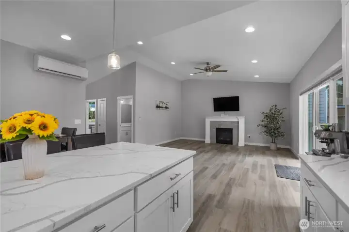 Open kitchen and Great Room view showcasing quartz counters, vaulted ceiling, fireplace, and slider access
