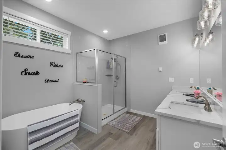 Luxurious primary bath with soaking tub, glass shower, double vanity, and quartz-style counters.