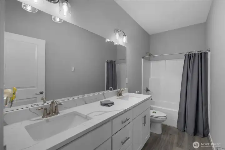 Guest bathroom with double-sink vanity, quartz-style counter, tub/shower, and updated finishes.