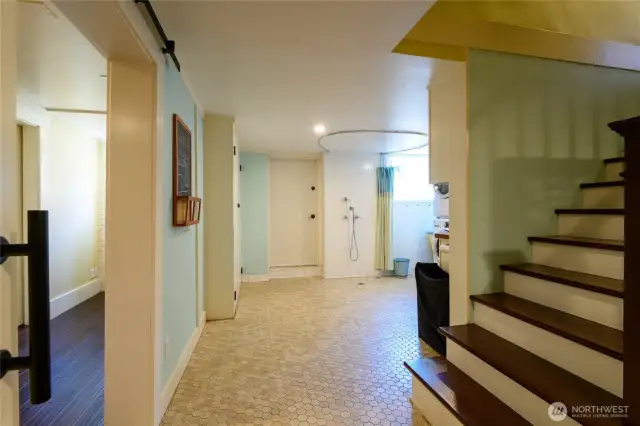 Heading down the steps from the kitchen, the daylight basement is where you'll find the media/rec room and laundry, as well as the 4th shower in the home. The open door to your left leads to the rec/media room, while the pup shower and laundry area are directly ahead. That door in the middle of the image leads to the back courtyard, while turning right past the steps takes you to the laundry room.