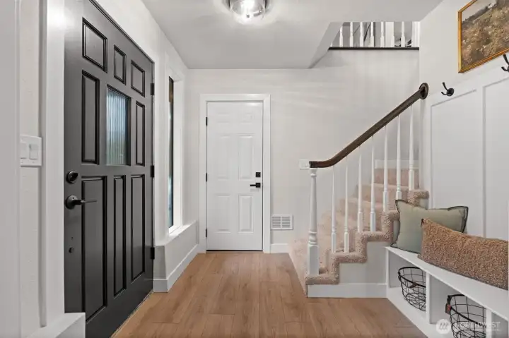 Bright, open ground-floor entryway with garage access, storage bench, and stairs leading up.