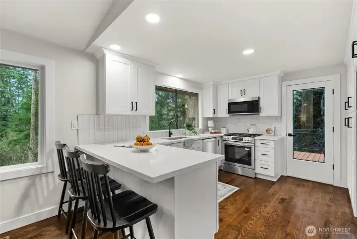 Bright, open kitchen featuring brand-new stainless steel appliances, sleek cabinetry extending to the ceiling, and an inviting breakfast bar—perfect for entertaining, casual dining, and gathering with friends.
