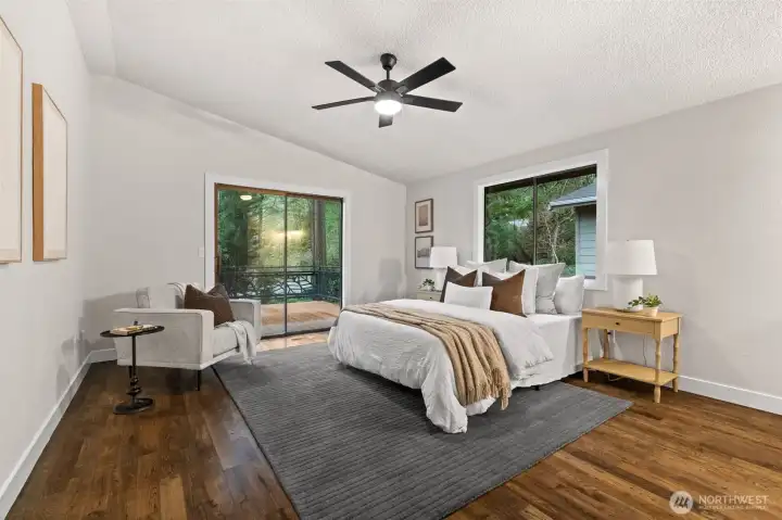 Vaulted primary suite featuring hardwood floors, ceiling fan, and private deck entry.