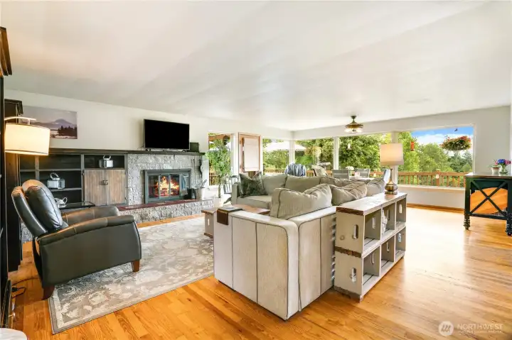 The stunning great room impresses with a dramatic wall of windows, gleaming hardwood floors, and a cozy wood stove—plus seamless access to the wrap-around deck for indoor-outdoor living at its finest.