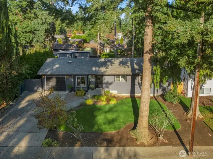 This listing features a spacious lot with lush landscaping, mature trees, and a paved driveway.