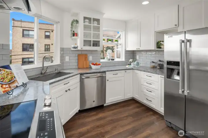 Tastefully an updated kitchen with a range hood, full height tile backsplash, slab quartz, newer custom cabinetry and appliances.  Light and bright with two windows!