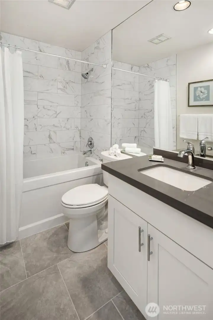 Guest bath has large soaking tub, beautiful 8 x 24 tile surround, new tile flooring, toilet and vanity/sink.