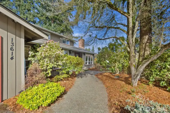 Landscaped front entry with curved walkway, mature trees, and established garden beds creating a welcoming approach to the home.