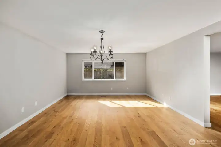 Bright dining room with statement chandelier, expansive hardwood floors, and open layout connecting to the main living areas.