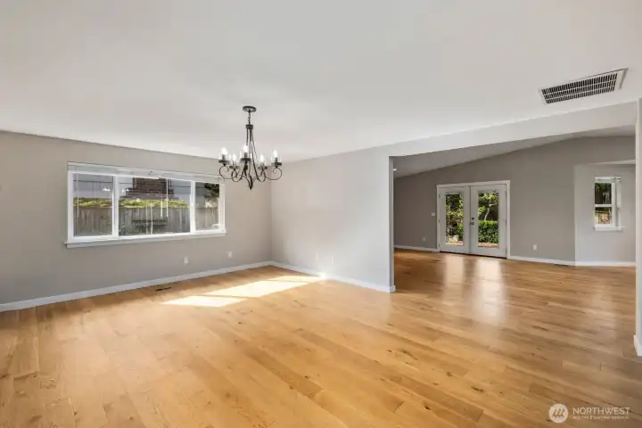 Dining area with large window overlooking the backyard, hardwood flooring, and open sightlines to the adjoining living space.