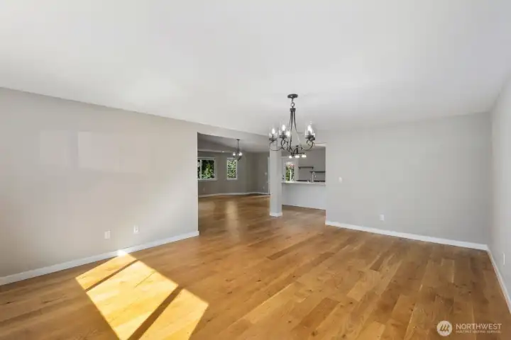 Spacious open-concept living and dining area with hardwood floors, modern chandelier, and seamless flow toward the kitchen.