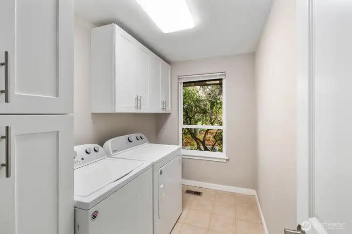 Dedicated laundry room with washer and dryer, upper storage cabinets, and window bringing in natural light.