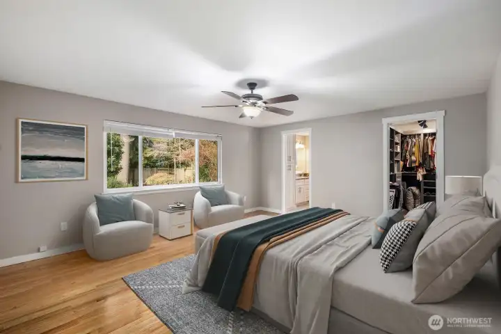 Virtually staged main floor primary suite with large windows, hardwood floors, and space for a sitting area.