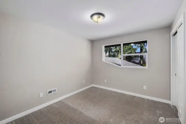 Comfortable bedroom with plush carpet, large window for natural light, and closet storage.