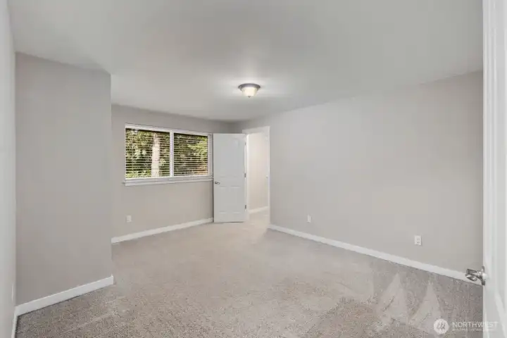 Spacious bedroom with soft carpeting, neutral walls, and large window bringing in natural light.