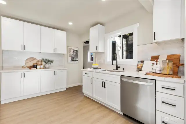 Another view of large kitchen with lots of white painted cabinets quartz counters ss appliances and ss under mount sink. There is beautiful white tile back splash behind all counters also.  The hallway leads to butlers pantry and east entry door from kitchen to back of home