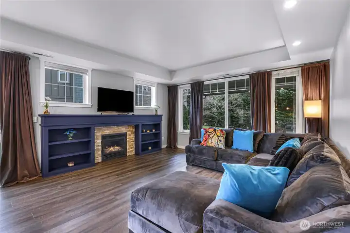 Cozy living room with a custom built fireplace surround and large windows showcasing the greenery outside.