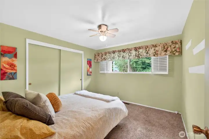 Generously sized bedroom featuring soft carpet underfoot, a large closet with sliding doors, and peaceful views out to mature trees. Calm wall color and ceiling fan contribute to a restful retreat at the end of the day.
