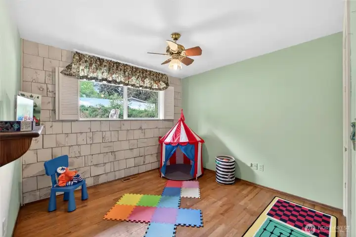 Sunny secondary bedroom currently styled as a playroom, with warm hardwood floors and a wide window overlooking the front yard greenery. Neutral wall tones and simple finishes make it easy to convert into a guest room, home office, or creative space. Nice sized closet.