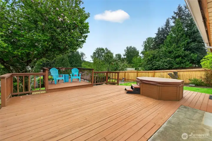 Spacious entertainment deck with built-in hot tub and multiple seating areas overlooking the private backyard