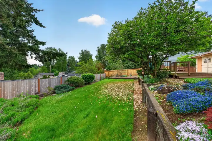 Private park-like backyard with mature landscaping, garden beds, and expansive green space that creates a peaceful outdoor setting.