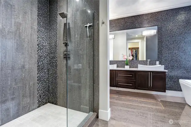 Huge walk-in shower with overhead rain shower. Mosaic accents floor-to-ceiling tile, frameless glass shower door, and inset shampoo niche. Walk-in closet is located behind the shower. You can see the reflection in the mirror.