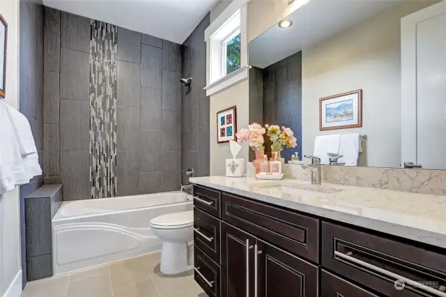 Upper floor main hall bath that serves the two bedrooms adjacent to it. Double vanities, tub-to-ceiling tile surround with vertical tile accents. Shampoo shelf at the foot of the tub.