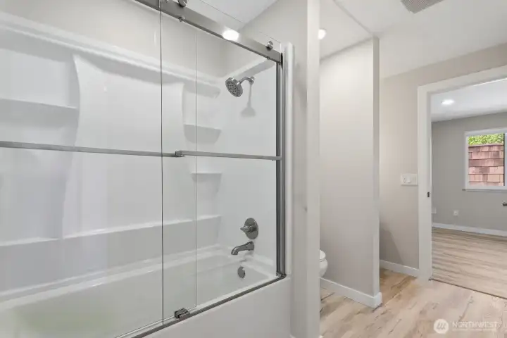Jack-and-jill bathroom connecting the guest bedroom and primary bedroom upstairs. Fully remodeled with new tub, shower doors, vanity, flooring and paint.