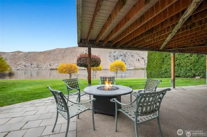 Covered outdoor patio with fire feature invites year-round enjoyment beside the peaceful waterfront setting.