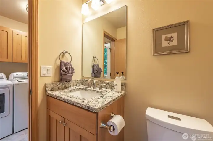 Convenient powder room with granite countertops and warm wood cabinetry adds style and functionality for guests on the lower level.