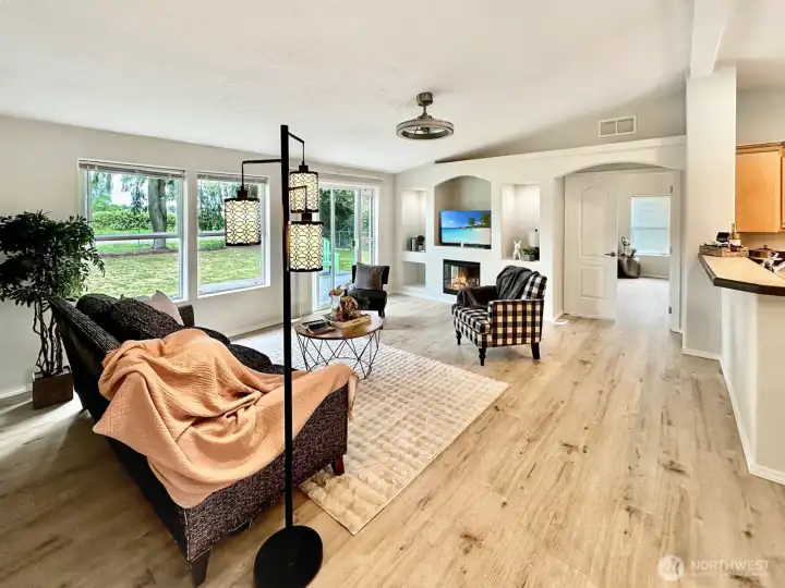 Lovely, vaulted living room with laminate floor, electric fireplace with display niches, ceiling fan and access to the rear yard, primary bedroom and kitchen via the pass through.