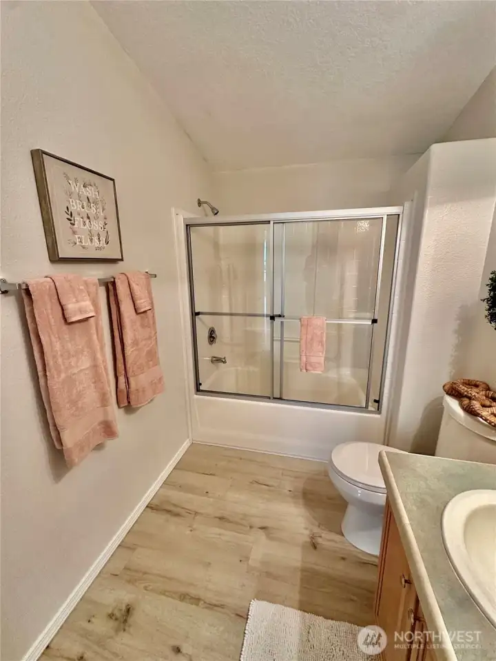Hall full bath with glass shower doors and laminate floor.