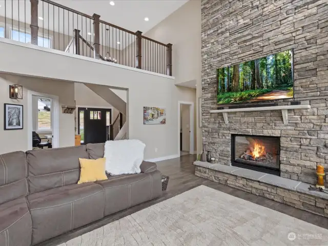 Spectacular Great Room with soaring ceiling, floor-to-ceiling stone fireplace & partial views.