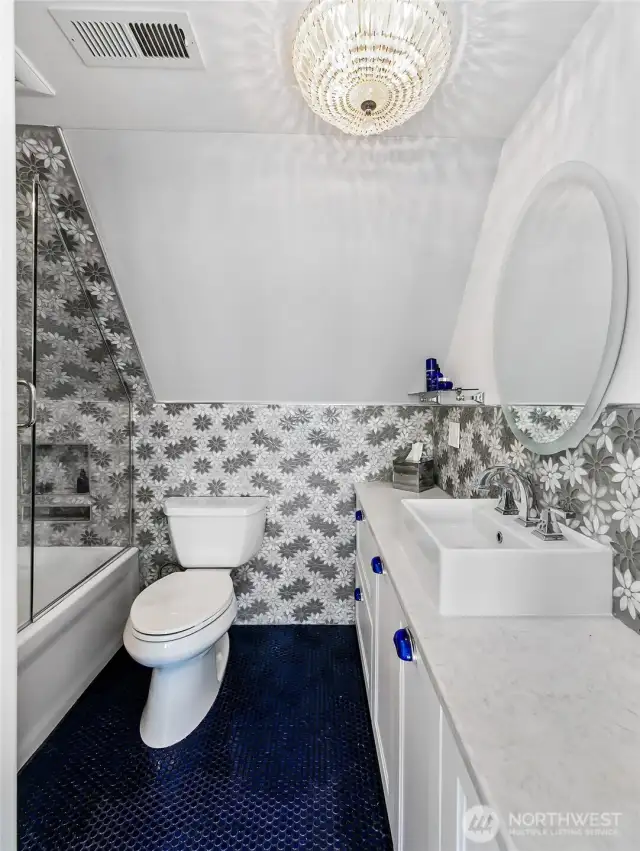 With a cascade of daisy tile, deep blue penny floor, and a crystal chandelier overhead, the upstairs bath offers both whimsy and refinement—tucked under the eaves like a secret spa.