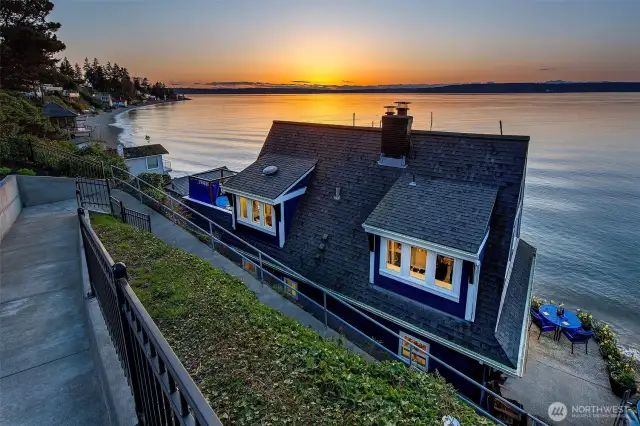 As you climb the quiet path above the shoreline, the roofline of Caledonia Cove slips gently from view, and the Browns Point Lighthouse glows in the distance—its beam a steady companion to the setting sun. Up ahead, the upland terrace waits, tucked in gardens and sea breeze, offering one last lingering look back across the water… and forward toward whatever’s next.