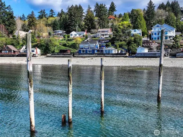 From the water, the home reveals itself like a secret—nestled among Browns Point’s hillside cottages and framed by weathered pilings, the last remnants of the old Mosquito Fleet dock that once connected these shores to the greater Sound. With its bold blue façade and cheerful yellow door, the home stands as a beacon of character and calm, its terraces cascading toward the tide like steps in a well-kept promise.