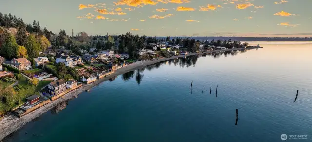 From this final vantage, the story of 7316 East Side Drive comes into full focus. The lovingly restored beach house, with its joyful accents of blue and yellow, hugs the shoreline like it was always meant to be there. Behind it, the upland terraces step upward in graceful layers—loungers catching the last of the day’s light, flowerbeds just beginning to bloom, and a pavilion waiting for laughter and shared meals.    Out in the water, the weathered pilings of the old Mosquito Fleet dock rise like sentinels, a reminder of the region’s maritime legacy. And just beyond, the Browns Point Lighthouse holds its place at the tip of the peninsula—steadfast, familiar, a beacon across generations.    This isn’t just a home. It’s a hymn to the Pacific Northwest. A place where land and water, past and present, solitude and connection all meet. Where every morning opens with light on the bay, and every evening closes with a painted sky.    Here, the long view isn’t just a perspective—it’s a w