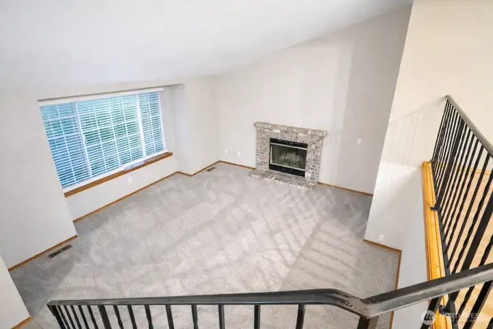 Spacious split-level living area featuring vaulted ceilings, exposed wood beams, and an open railing overlooking the kitchen. Soft carpet, durable tile flooring, and abundant natural light create a warm, functional layout with easy flow between levels—ideal for flexible living and entertaining.